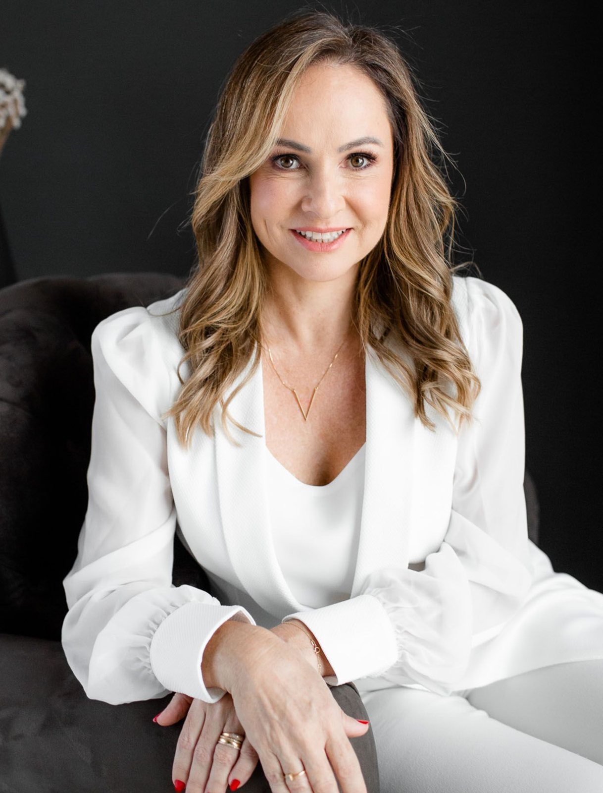 Dra. Alessandra Nalin, de blazer branco, sentada em fundo escuro